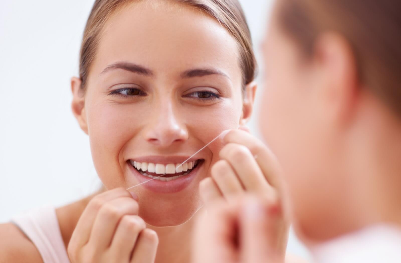 A person looking in the mirror while flossing their front teeth and smiling.