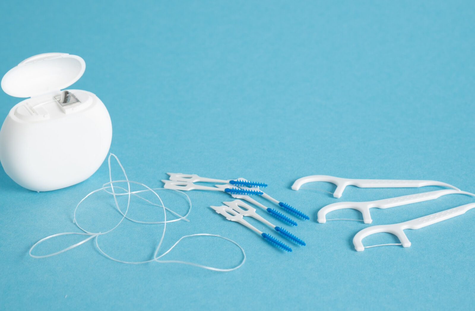 A number of flossing tools against a blue background, including regular floss, interdental brushes, and floss picks.