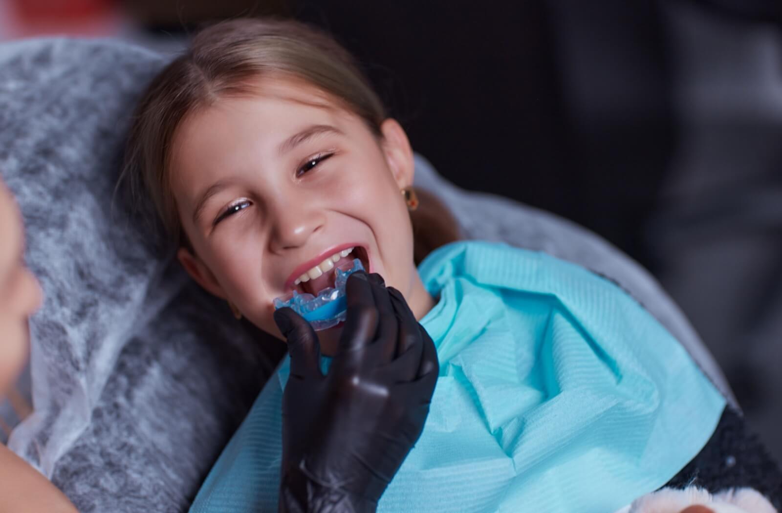 A pre-teen smiles as an orthodontist places a mold into their mouth that will create a unique Invisalign for their teeth.