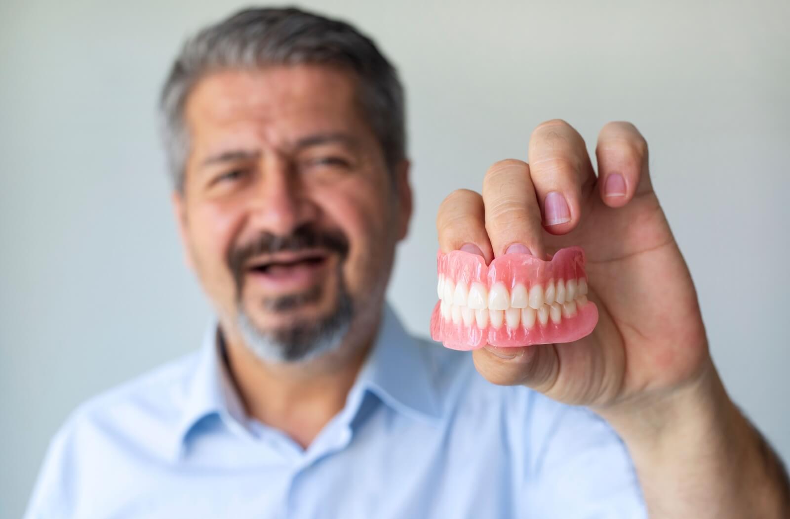 A man holding a set of dentures and smiling.