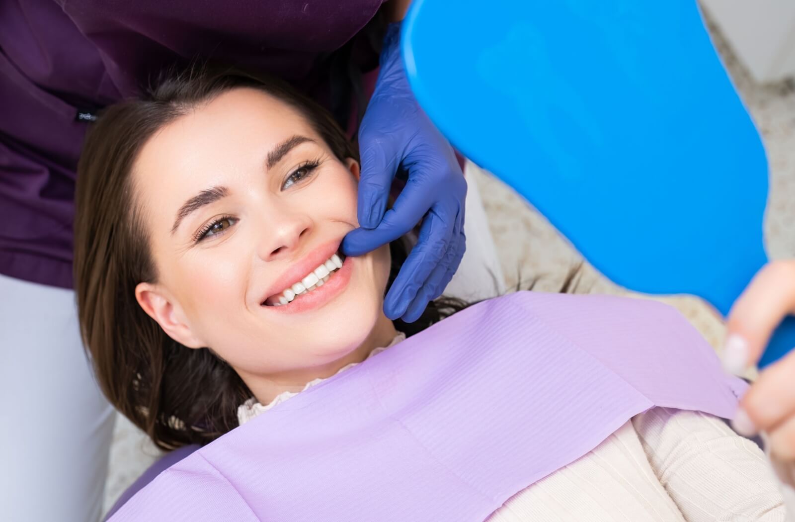 Someone is shown the results of their teeth whitening treatment at the dentist office, and they are smiling happily.